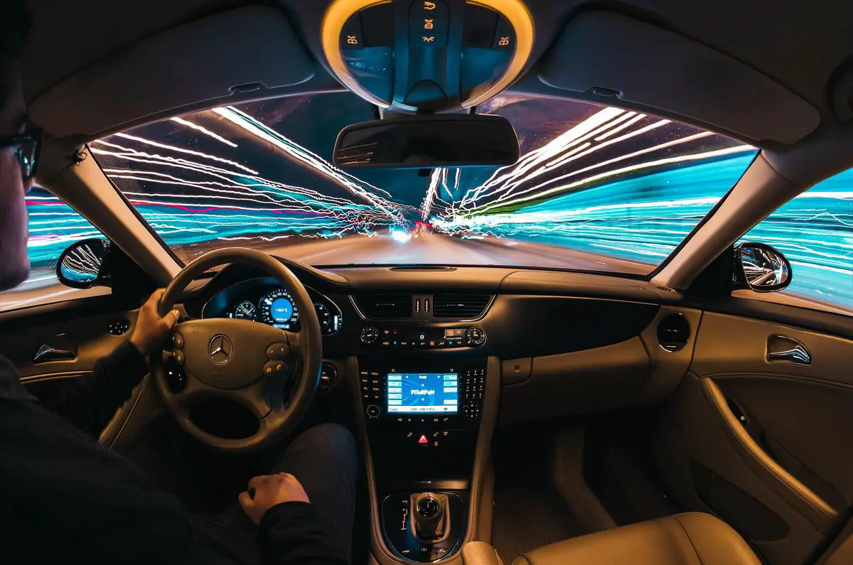 Image of a self-driving car being tested on a road with a scientist monitoring it from the sidewalk.